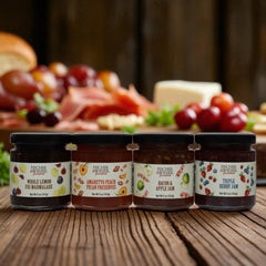 Four jars of Fischer & Werner preserves on a wooden surface with a platter of food in the background.
